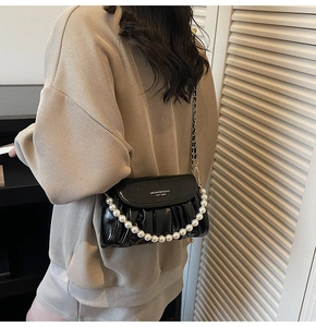 Detail of black glossy pleated crossbody bag with large pearl handle and metal chain strap