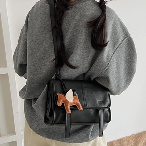 Detail of black matte leather shoulder bag with a horse charm and decorative straps