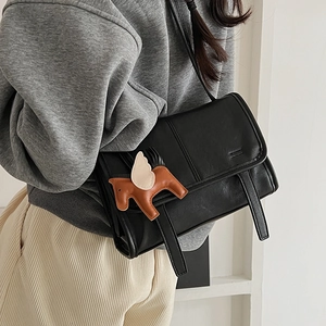 Detail of a black matte leather crossbody bag featuring a brown winged horse charm