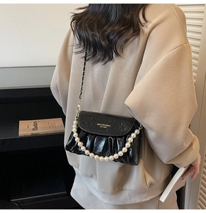 Close-up of black pleated bag with pearl handle and gold chain strap on model