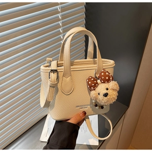 Detail of creamy white bucket bag with pebble leather texture and cute plush bear charm