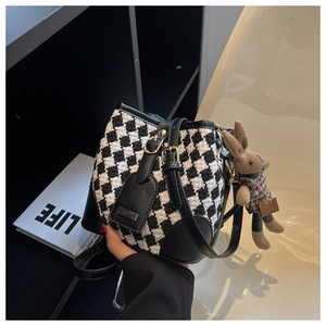 Detail of houndstooth bucket bag with a plush bunny charm and adjustable leather strap