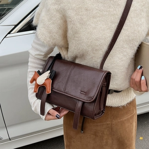 Brown leather crossbody bag with a horse charm shown on a model in a casual outfit