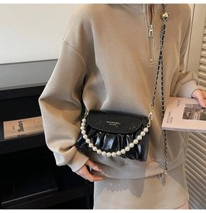 Detail of a black glossy pleated crossbody bag featuring a large pearl chain and gold logo