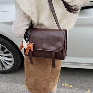 Brown leather messenger bag with decorative vertical stitching and small horse pendant detail