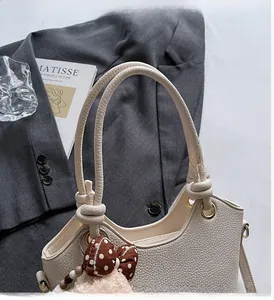 Close-up of off-white lychee grain leather bucket bag with knotted handle and charm