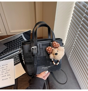 Detail of denim bucket bag with leather trim and plush bear charm on a desk