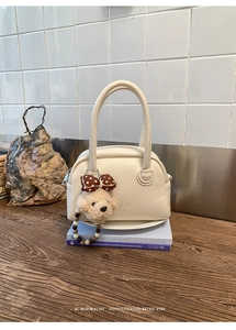Dettaglio borsa bowling in pelle crema con ciondolo a forma di cucciolo su libro