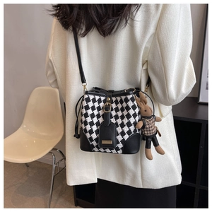 Detail of checkerboard bucket bag with brown rabbit charm and slim leather strap