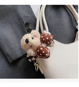 Close-up of a plush bear bag charm with brown polka dot bow on white leather purse