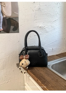 Dettaglio borsa bowling in pelle nera con ciondolo a cucciolo su piano di legno