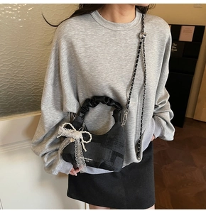 Detail of black textured handbag featuring cloud pleated handle and pearl lace bow charm