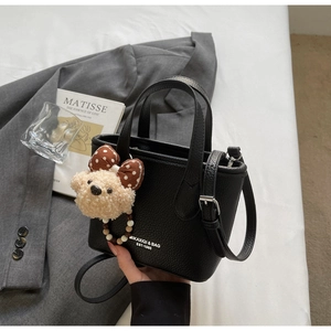 Detail of black pebbled leather bucket bag with brand logo and cute bear charm