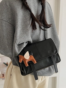 Minimalist black flap shoulder bag with decorative straps and a horse charm accessory