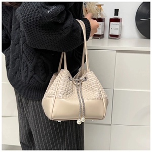 Detail der beigen Flecht-Eimertasche mit silbernem Kettenzug und Perlenverzierung