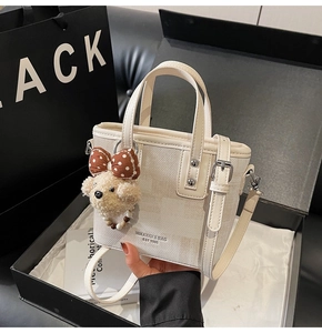 Detailed shot of cream crossbody bucket bag with plush bear charm and gift packaging