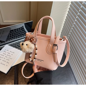 Detail of pink crossbody bucket bag with litchi leather texture and bear charm