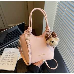 Detailed view of pink pebble leather bucket bag with knot handle and teddy bear charm