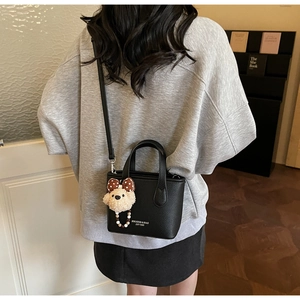 Detail of black pebbled leather bucket bag with cute bear charm and logo print