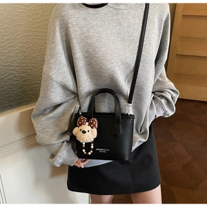 Close-up of black lychee leather bucket bag with a plush bear charm and crossbody strap
