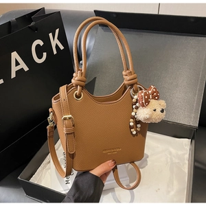 Detail of brown litchi grain bucket bag with cute bear charm and golden hardware accents