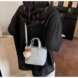 Detail view of light blue litchi pattern bucket bag with cute plush bear charm on model