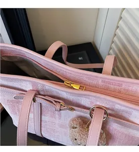 Detalle de la cremallera dorada y el asa de cuero rosa del bolso tote con diseño de cuadros
