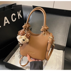 Detail of brown litchi leather bucket bag with knotted handle and plush bear charm