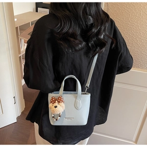 Detailed back view of a light blue textured leather bucket bag with a plush bear charm