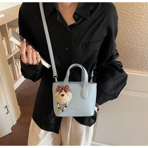 Detail of light blue bucket bag featuring litchi texture and cute teddy bear pendant
