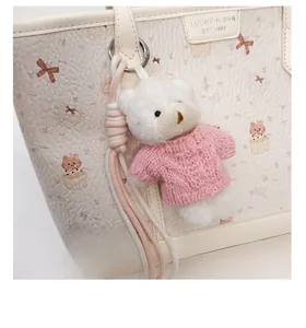 Detail of cute plush bear charm with pink knit sweater on a printed tote bag