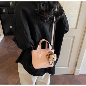 Detail of pink lychee leather bucket bag featuring a cute teddy bear charm with polka dot bow