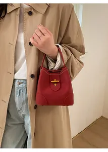 Detail of red bucket bag featuring golden cross lock and elegant lychee grain texture