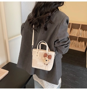 Crossbody view of cream woven bucket bag with adjustable strap and plush bear charm