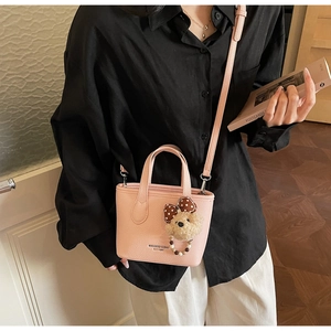 Detail of pink faux leather bucket bag with bear charm and adjustable shoulder strap