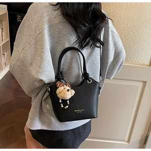 Detail of black pebbled leather bucket bag featuring a plush bear charm and gold lettering