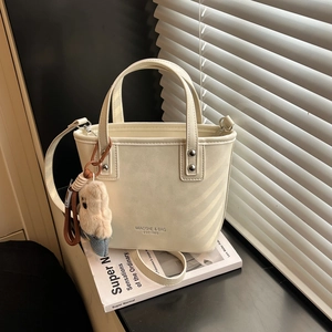 Beige tote bucket bag with bear pendant shown under natural window blind shadows