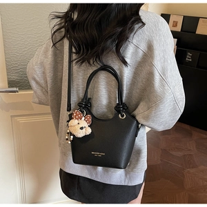 Close-up of black lychee grain bucket bag with brand logo and cute teddy bear charm