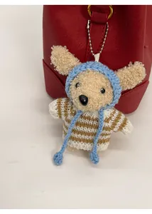Plush animal bag charm with blue knit hat and striped sweater on a red leather bucket bag