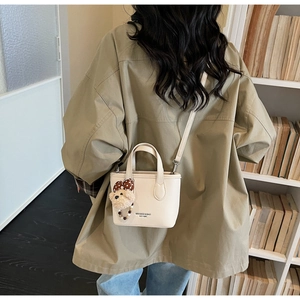 Detail of cream white leather bucket bag with cute plush bear pendant and logo print