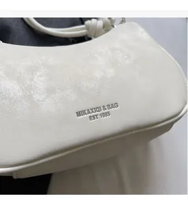 Macro detail of white pleated faux leather shoulder bag with a knotted strap and silver logo