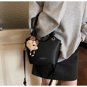 Detail of black lychee grain bucket bag with gold hardware and plush bear charm decoration