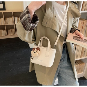 Detail of a creamy white leather bucket bag with a cute brown teddy bear pendant charm