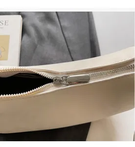 Detailed close-up of the smooth silver metal zipper and cream leather texture of the bag