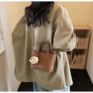 Brown leather tote bag with charm shown on shoulder for daily commute style