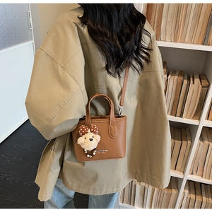 Brown litchi grain leather bucket bag with cute bear charm worn over the shoulder