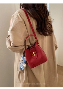 Detail of red pebbled leather bucket bag featuring a gold metal clasp and a bear charm