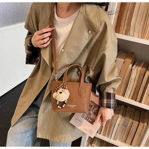Detail of brown litchi pattern leather bucket bag with teddy bear pendant on bookshelf