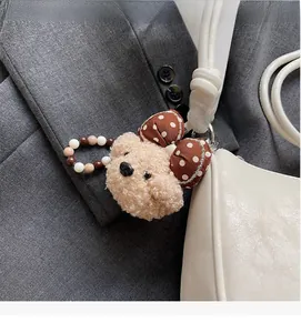Detail of cute teddy bear plush charm with polka dot bow on a white leather handbag