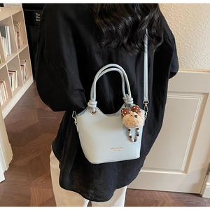 Close-up of light blue bucket bag with litchi grain and cute plush bear charm